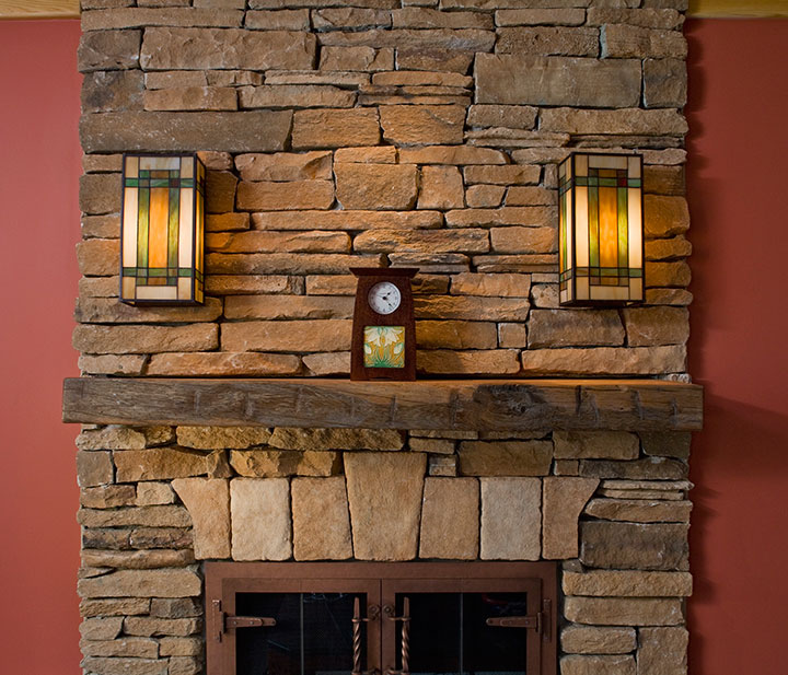 FIREPLACE WITH STONE CLADDING, RECLAIMED MANTEL AND STAINED GLASS SCONCE LIGHTS.